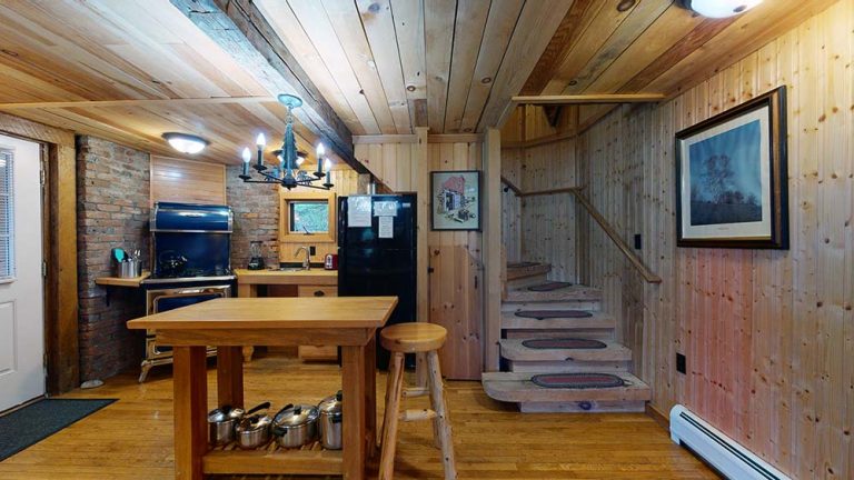 Rustic kitchen and dining area with wooden walls, brick accents, and a staircase.