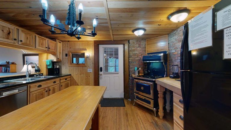 Cozy rustic kitchen with wooden cabinets, long island, brick wall, and blue stove area.
