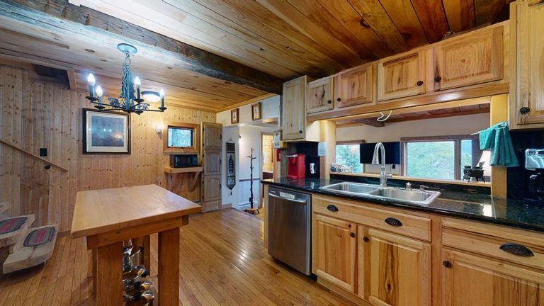 Rustic wooden kitchen with island, exposed beams, and granite counters under warm lighting.