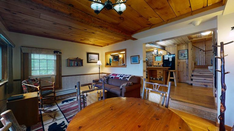 Cozy rustic living area with wood ceiling, sofa, dining table, and doorway to kitchen in cabin-style home.