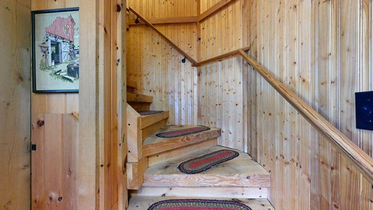 Wood-lined staircase in a log cabin hallway with colorful runners and wooden railings.