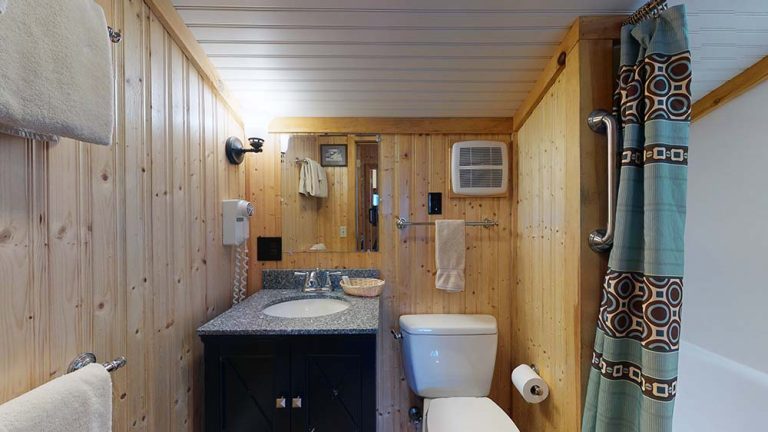 Cozy wooden bathroom with vanity, mirror, toilet, towel rack, and patterned shower curtain.