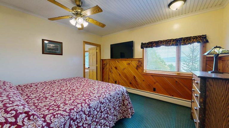 Bedroom with two twin beds, wood paneling, dresser, window, TV, ceiling fan.
