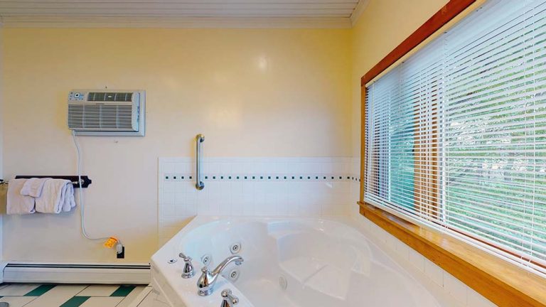 Bathtub with wall tile, window blinds, and wall AC in a yellow bathroom.