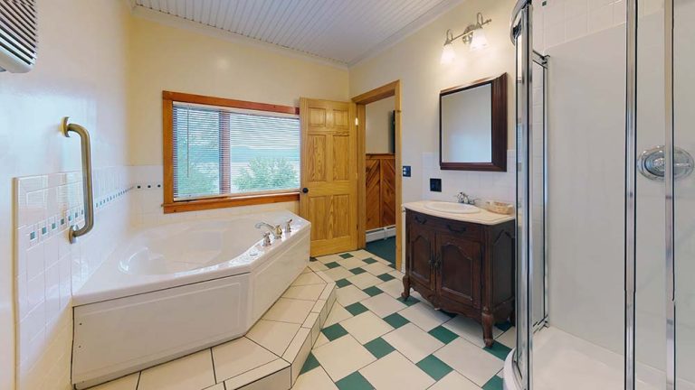 Bathroom with corner tub, vanity, shower, window, and checkered green-white floor.