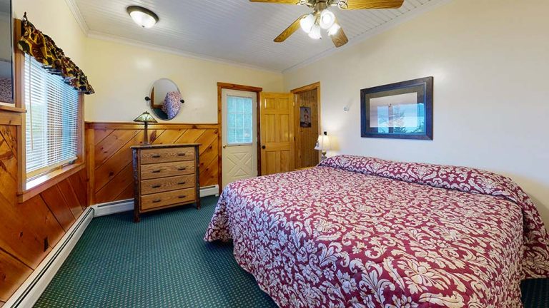 Cozy bedroom with two large beds in burgundy and white floral bedspreads, wood paneling, dresser, mirror, window, and ceiling fan.