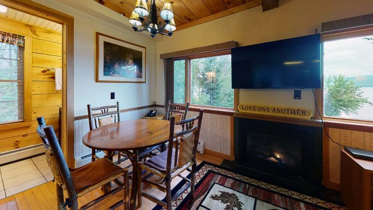 Cozy wood-paneled dining room with round table, chairs, fireplace, and mounted TV.