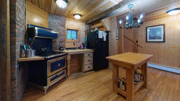 Rustic kitchen with wood walls, brick accents, black-blue vintage oven, sink, fridge, island.