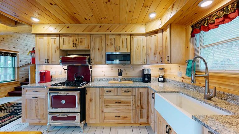 Rustic wood kitchen with granite counters, stainless stove, sink, and window.