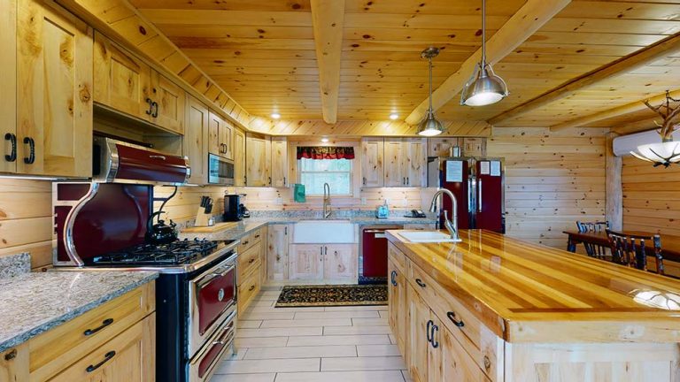Rustic kitchen with wooden cabinets, island, stainless appliances, red fridge, and pendant lights.