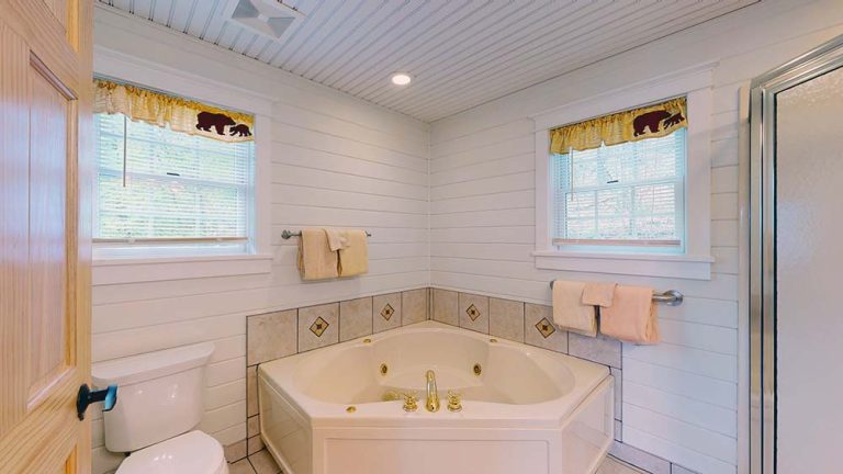 Bright white bathroom with a corner tub, tiled backsplash, and two windows.