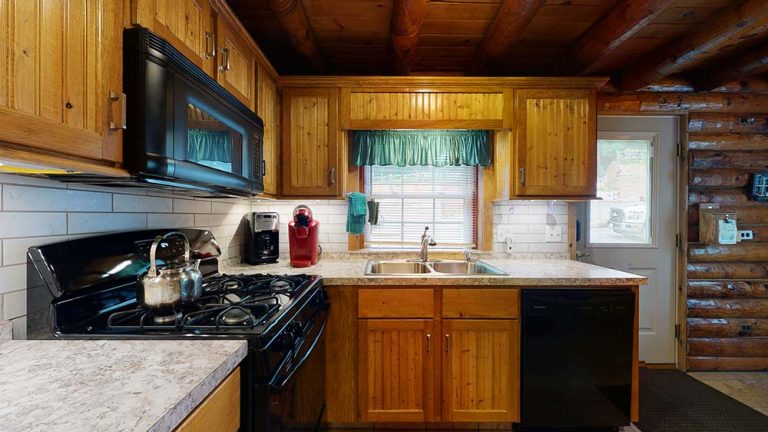 Cozy wooden kitchen with gas stove, kettle, coffee maker, red espresso machine, window, and sink.