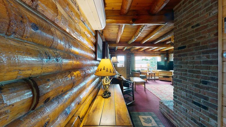 Cozy log cabin living room with wooden walls, brick fireplace, and seating area.