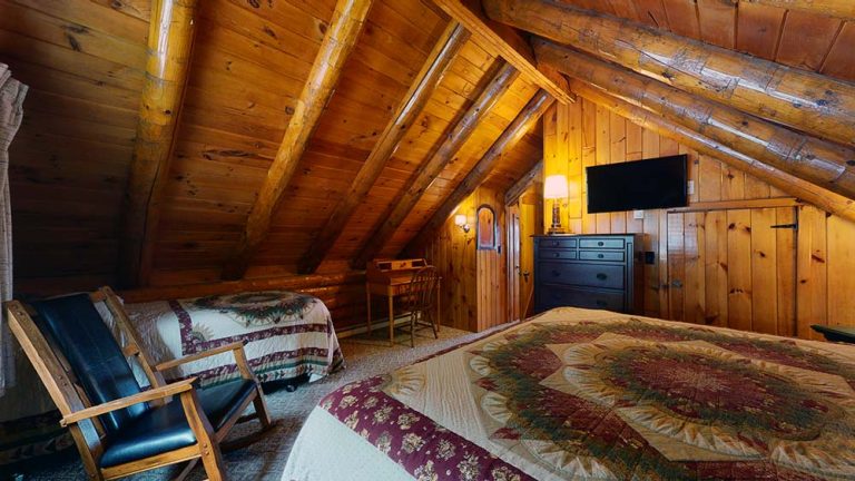 Cozy attic bedroom with wood paneling, two beds, a dresser, and warm lighting.