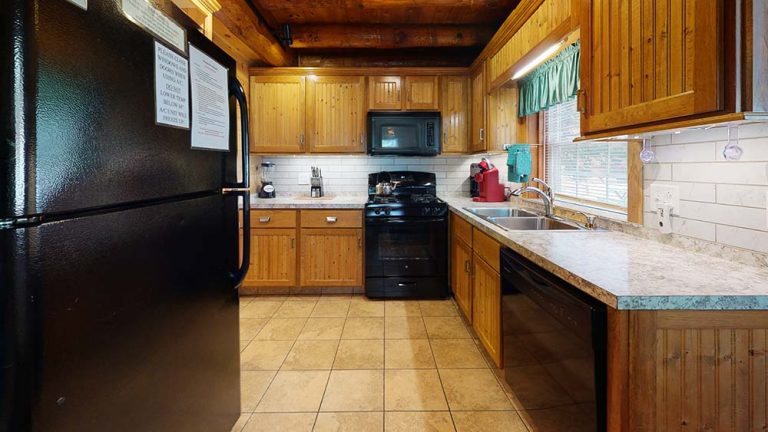 Wooden kitchen with black appliances, white backsplash, and a double sink under a window.