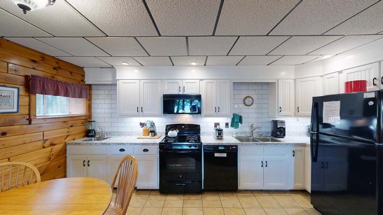 Bright white kitchen with white cabinets, black appliances, wooden wall, and round table.