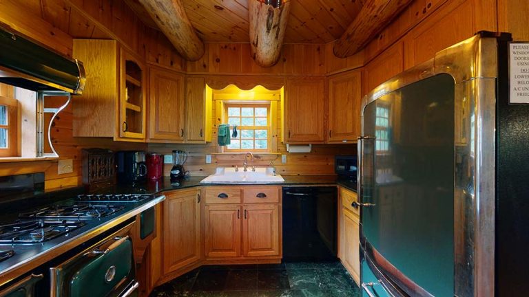 Rustic wood kitchen with curved shelf, green fridge, stove, sink, and warm cabin lighting.
