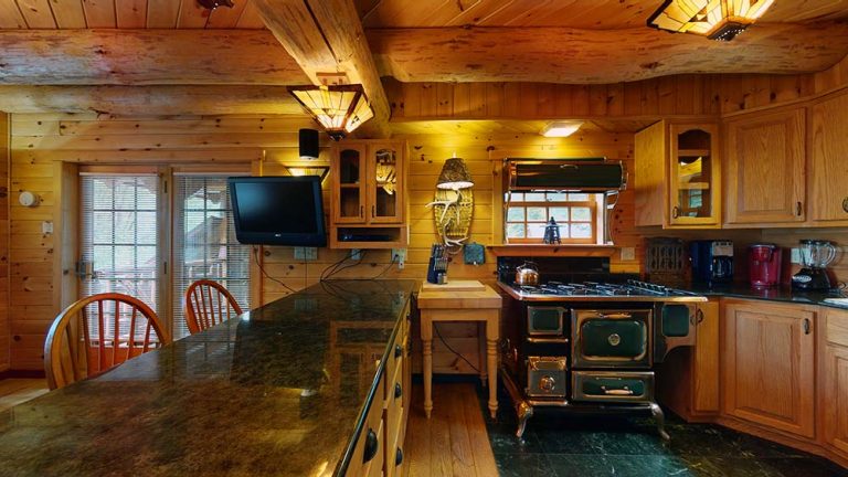 Rustic cabin kitchen with green vintage stove, wooden cabinets, and granite island.