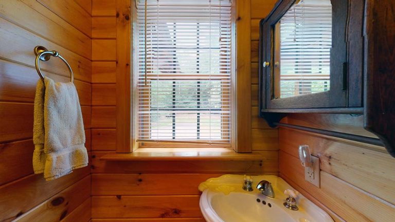 Small wooden bathroom with towel ring, window blinds, sink, and dark wall cabinet.
