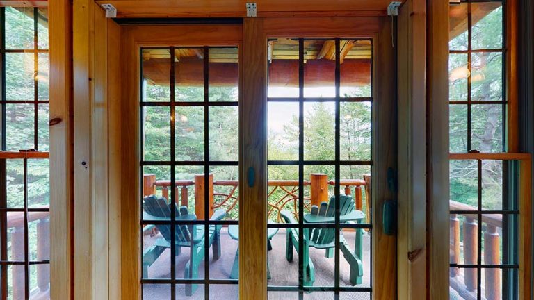 Glass-paned door opening to a wooden porch with green Adirondack chairs and railing.