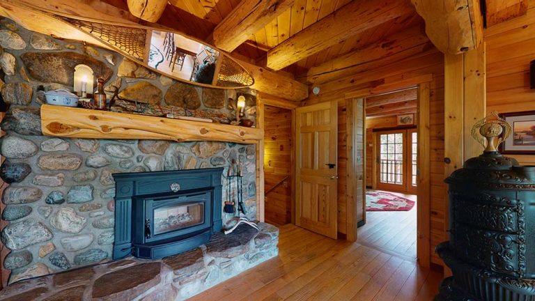 Cozy stone fireplace in a rustic wood cabin with a blue insert stove and wooden beams.