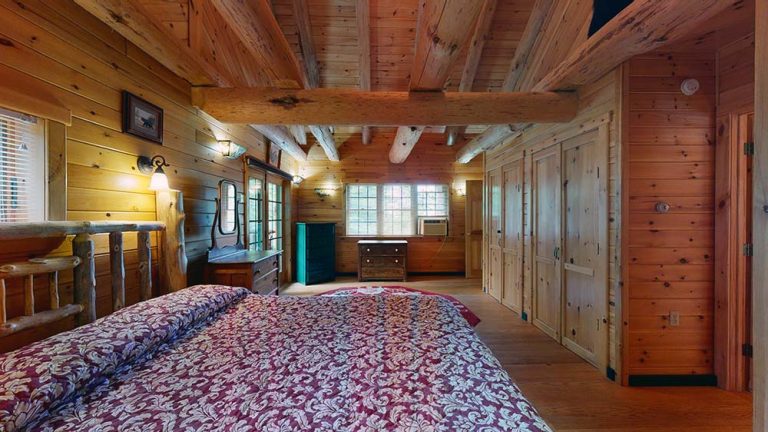 Rustic wooden bedroom with exposed beams, large bed, and built-in closets along one wall.