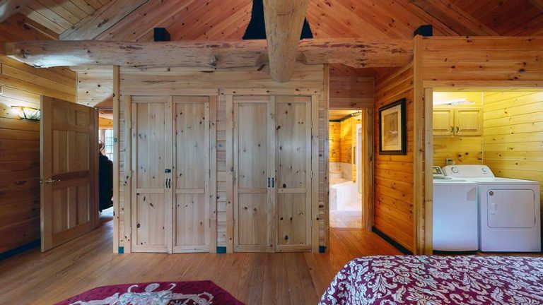 Wood-paneled cabin interior with closets, doorway, laundry area, and a bed in foreground.
