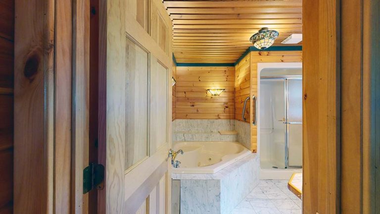 Wood-paneled bathroom with marble tub, glass shower, and exposed ceiling beams.