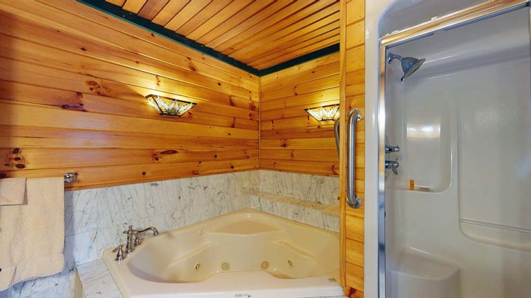 Bathroom with corner jetted tub, marble surround, wood paneled walls, and a glass shower.