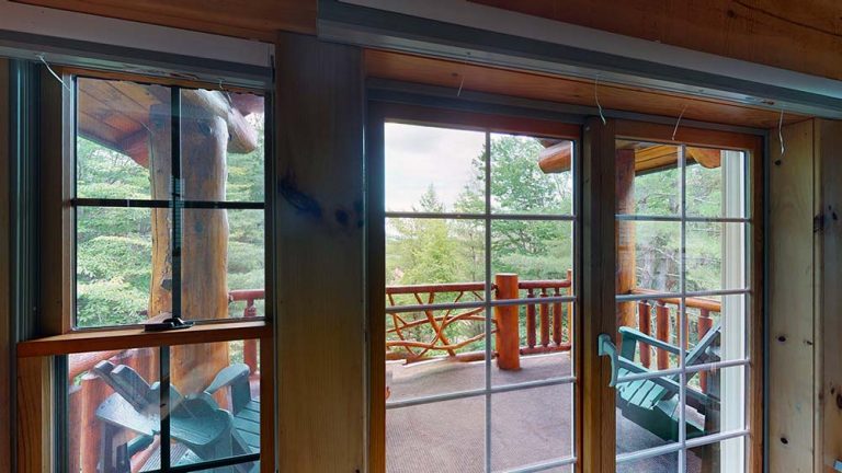 View from inside a wooden cabin onto a deck with green Adirondack chairs and railing.