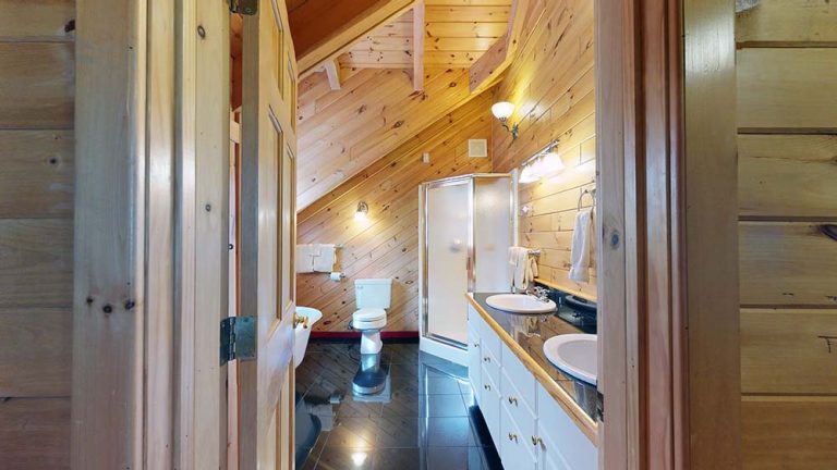 Rustic bathroom with wood paneling, double sinks, shower, toilet, and warm lighting.