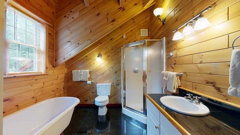 Wood-paneled bathroom with clawfoot tub, toilet, glass shower, and sink counter.